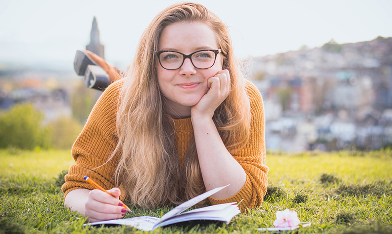 A young woman lays in the grass drawing, Homeschool vs. public school, pros and cons.