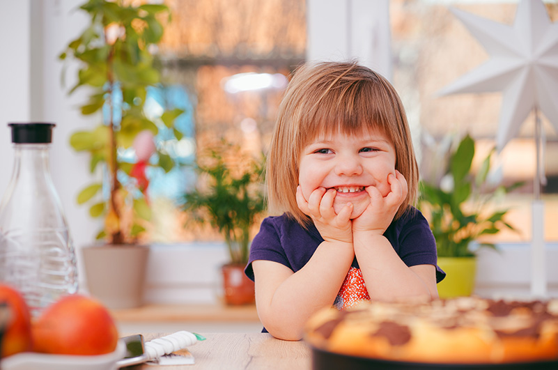 A young blond girl smiles in a kitchen.